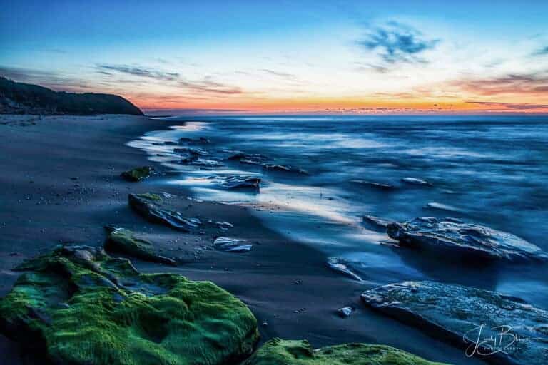 Red Bluff lakes Entrance Gippsland Australia at sunrise. The water is dark and the moss on the rocks is highlighted in the front of the picture