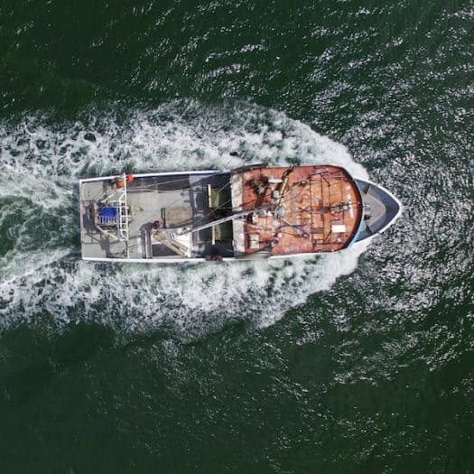 while flying a drone in gippsland you can capture an epic shot of a boat from above. This one is a trawler and it has the white wash from it's engines coming out the back in a beautiful shape around the boat
